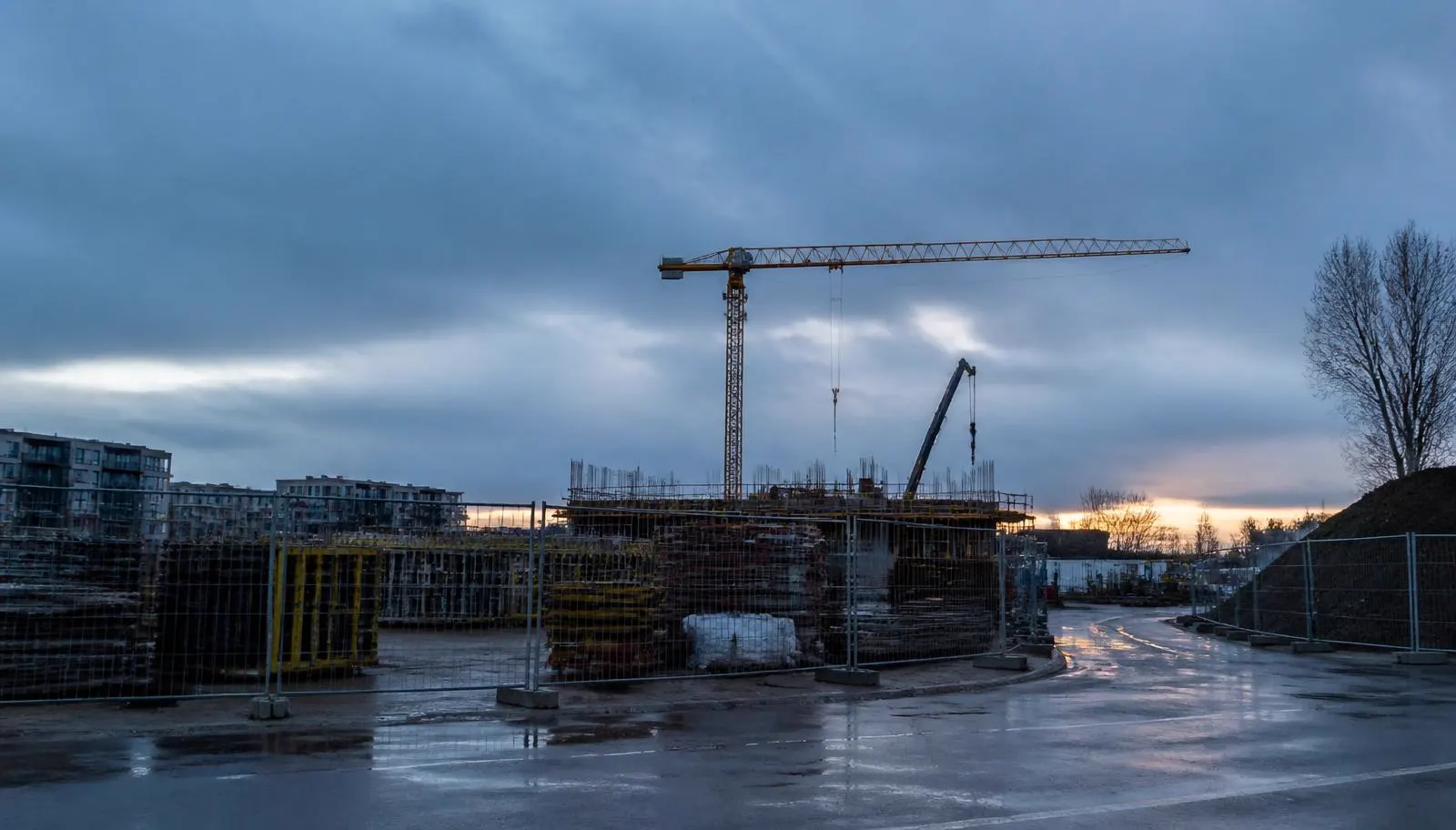 Umzäunte Baustelle mit Kran in der Dämmerung